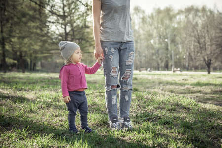 Child with mother walking together with holding hands in summer park on grass. Main subject is child. Unrecognizable mother on photo.  Concept for togetherness and care.の写真素材