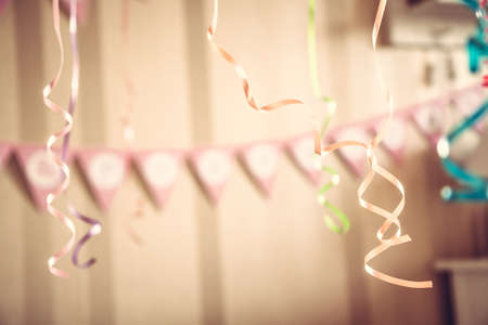 Vintage happy birthday party blurred background with hanging ribbons and garland in decorated room in pastel colorsの写真素材