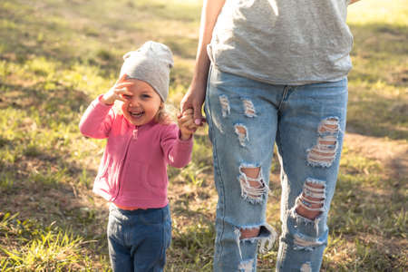 Playful child with mother walking together with holding hands in summer park on grass. Main subject...