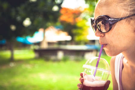 Woman quenching her thirst with refreshing cold drink in hot summer day in parkの写真素材
