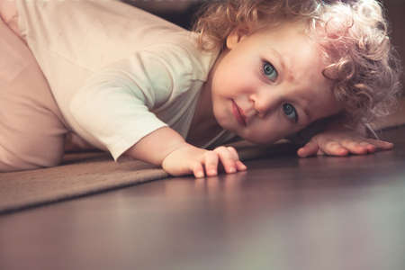 Curious cute child hiding under the bed in kids room and looking scaredの写真素材