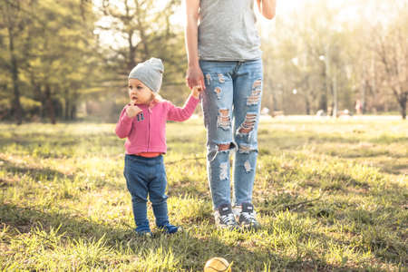 Child with mother standing together with holding hands in summer park on grass. Main subject is child. Unrecognizable mother on photo.  Concept for togetherness and care.の写真素材