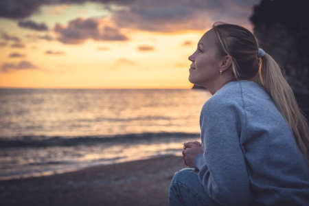 Pensive lonely smiling woman looking with hope into horizon during sunset at beachの写真素材