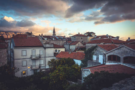 Old European city skyline with orange tile roofs and dramatic sky in antique architecture with trees in old European town Budva in Montenegro during sunsetの写真素材