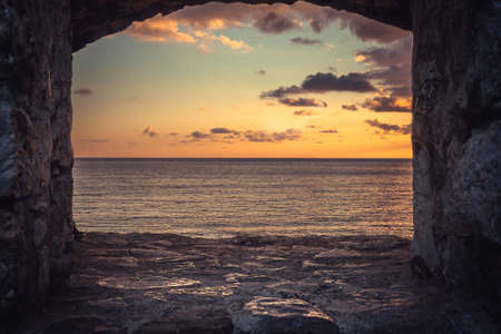 View of beautiful sunset over sea through window of old building with dramatic sky and perspective view.の写真素材