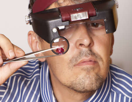 Male jeweler looking through a magnifier to check for flaws in a ruby   Focus on rubyの写真素材