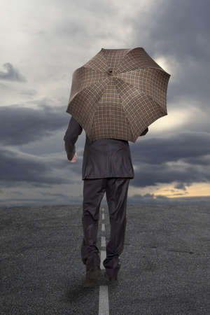 Businessman with umbrella under a stormy sky の写真素材