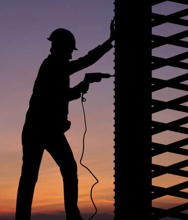 Silhouette of construction worker against sunset sky の写真素材