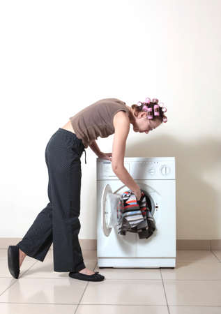 The woman with hair curlers adds garment to washing machineの写真素材