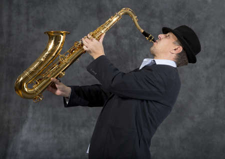 Portrait of a man playing on saxophone on grey background の写真素材