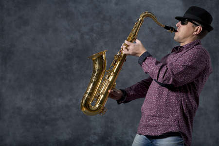 Middle-aged man playing on saxophone on grey backgroundの写真素材