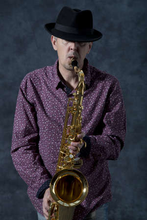 Saxophonist  Middle aged man playing on saxophone on grey backgroundの写真素材