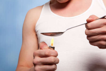 Man with a hardline drug addiction heating drugs in a spoon over a flame の写真素材