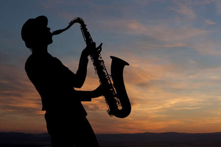 Saxophonist. Woman playing on saxophone against the background of sunsetの写真素材