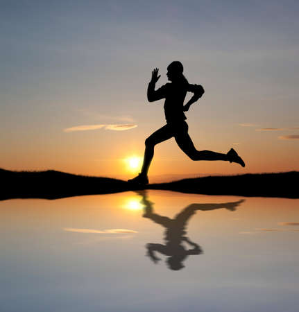 Silhouette of a fit woman running at sunset. Water reflectionの写真素材