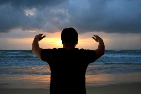 Man with his hands up on the dawn on the beachの写真素材