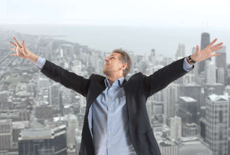 Happy businessman standing on the rooftop of a skyscraper over a cityscapeの写真素材