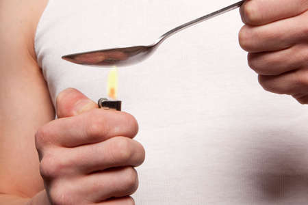 Man with a hardline drug addiction heating drugs in a spoon over a flame