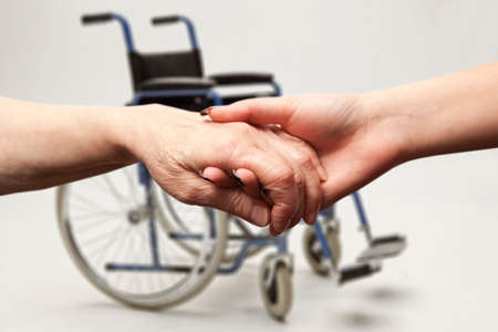 Hands of an elderly woman holding the hand of a younger woman on wheelchair backgroundの写真素材