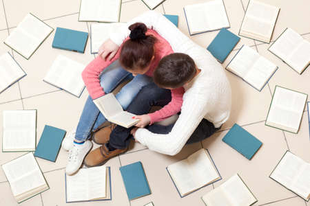 Young couple lying on floor with books and reading, top viewの写真素材