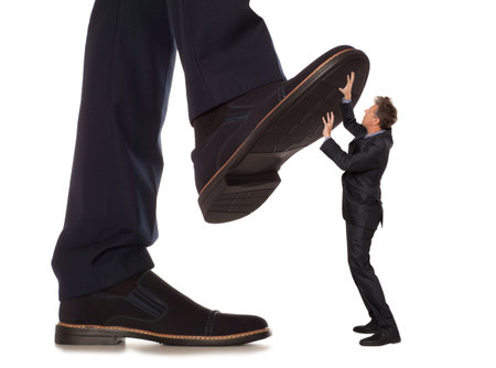 Cared small businessman under big leg his boss, isolated on white backgroundの写真素材