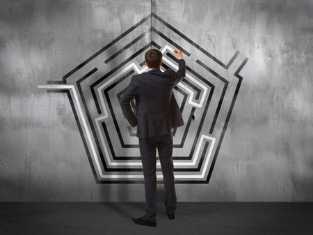Business concept. Back view of businessman drawing labyrinth on wall