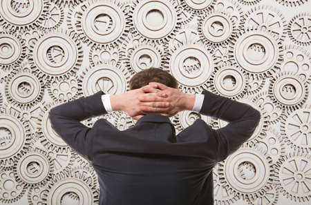 Back view of businessman looking at mechanism of cogwheelsの写真素材