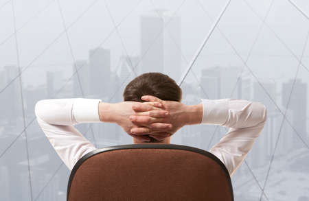 Businessman sitting in office and looking in cityの写真素材