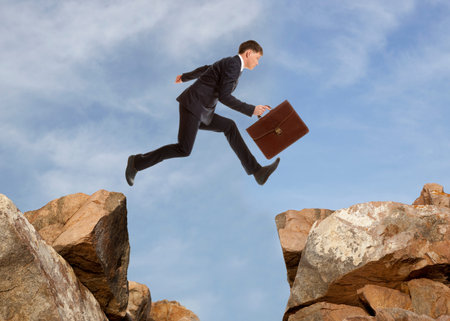 Young businessman jumping over rocks with gap concept