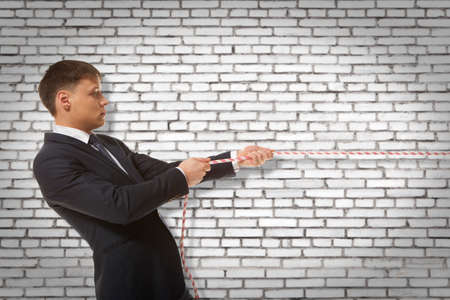 Businessman pulling a rope on wall backgroundの写真素材