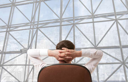 Businessman sitting in office and looking in cityの写真素材