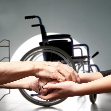 Hands of an elderly man holding the hand of a younger woman on wheelchair backgroundの写真素材
