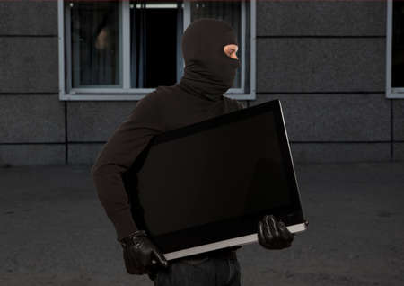Thief with balaclava stealing computer monitor or televisionの写真素材