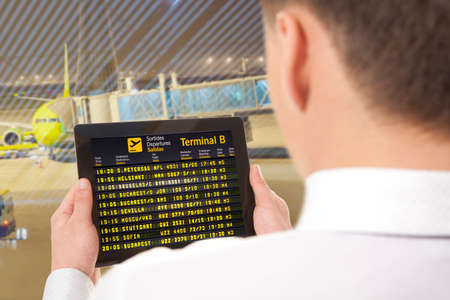 Businessman with tablet in airport with flight schedule and departure and gate informationの写真素材