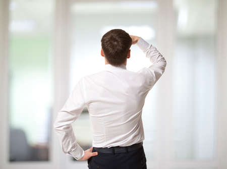 Thinking businessman in the office looking through the windowの写真素材