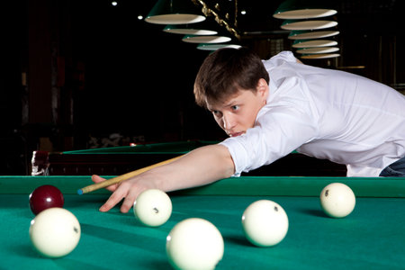 Young man playing billiards in the dark billiard club