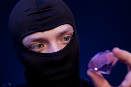 Thief. Man in black mask with a big emerald over dark blue background
