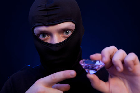 Thief. Man in black mask with a big emerald over dark blue background