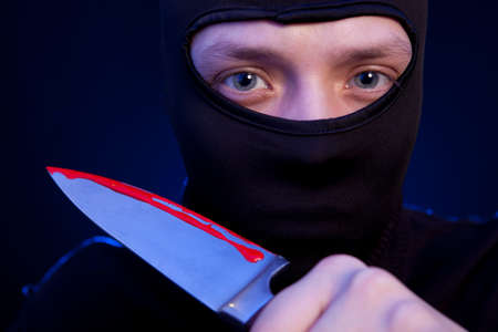 Man criminal in black mask with knife over dark blue backgroundの写真素材