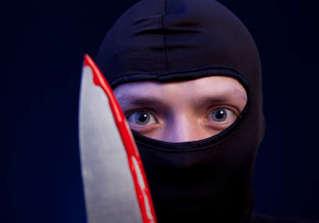 Man criminal in black mask with knife over dark blue backgroundの写真素材