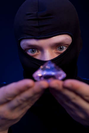 Thief. Man in black mask with a big emerald over dark blue backgroundの写真素材