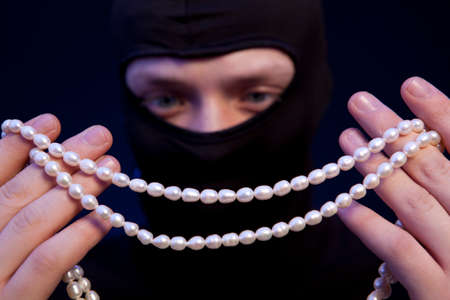 Thief. Man in black mask with a pearl necklace over dark blue backgroundの写真素材