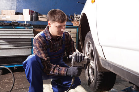 Car mechanic screwing or unscrewing car wheel of lifted automobile by pneumatic wrench at repair...