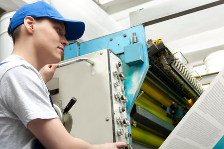 Young man in cap working in newspaper factory