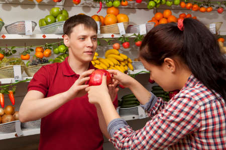 Young woman buys grapefruit. Assistant helping customer at vegetable counter of farm shopの写真素材