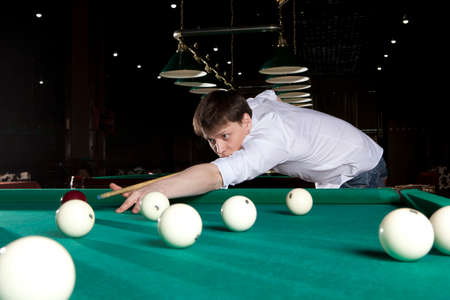 Young man playing billiards in the dark billiard clubの写真素材