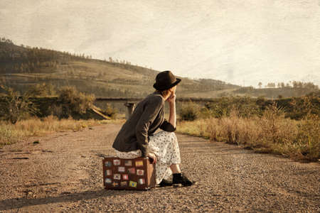 Women with vintage travel suitcase at old road. Photo in old image styleの写真素材