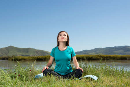 Young woman is practicing yoga at mountain river, relax in natureの写真素材