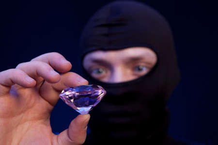 Thief. Man in black mask with a big emerald over dark blue backgroundの写真素材