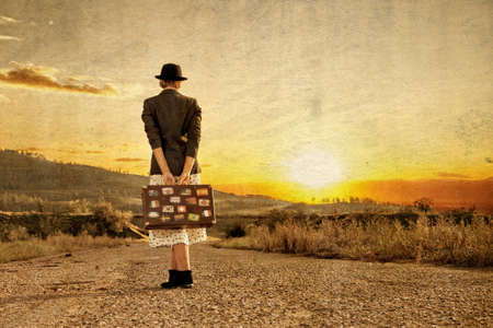 Women with vintage travel suitcase at old road. Photo in old image styleの写真素材